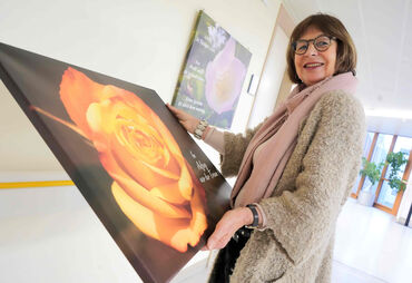 Frau mit großem Bild aus Leinwand in der Hand, darauf ist eine Rose zu sehen.