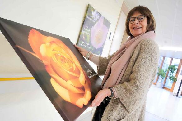 Frau mit großem Bild aus Leinwand in der Hand, darauf ist eine Rose zu sehen.